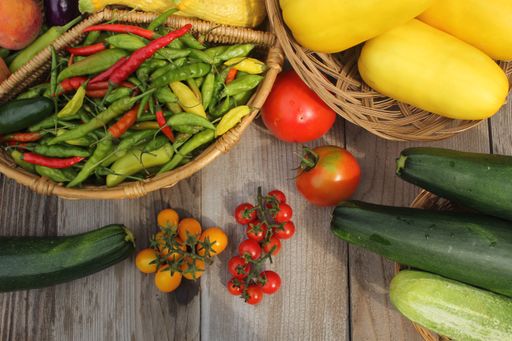 A top view of a fresh harvest of zucchini, peppers, cherry tomatoes, and pumpkins on the wooden table