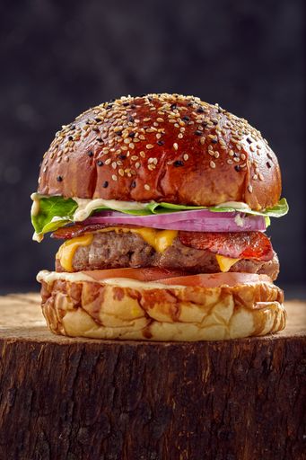 A vertical closeup of a burger on the stump with dark blurred background