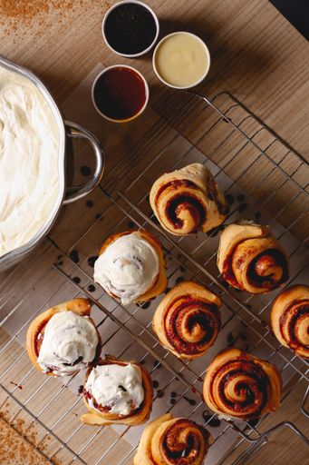 A vertic shot of hot, delicious Cinnabons on the table and a bowl with cream next to them
