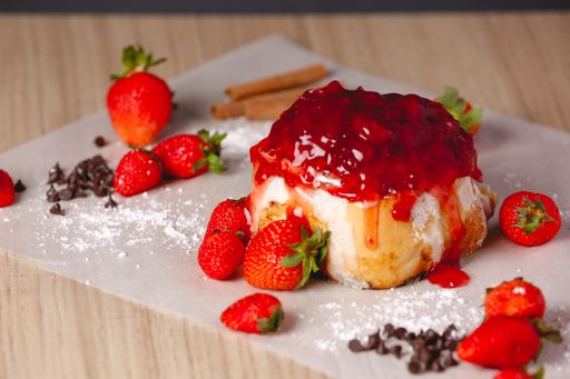 A closeup shot of a delicious Cinnabon on the table with cream and jam on top with berries