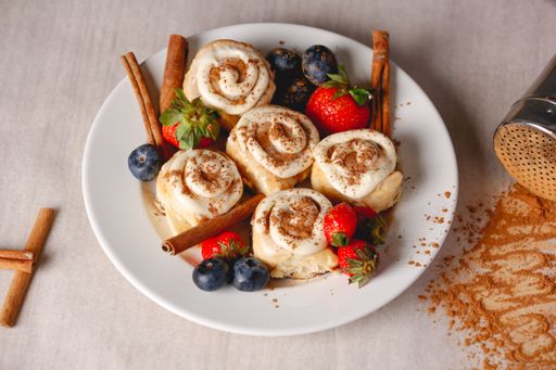 A closeup shot of delicious Cinnabons on the plate decorated with cinnamon sticks and berries