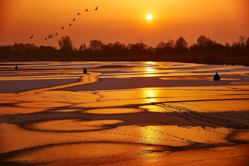 A beautiful shot of a large watered field with a few wooden huts and amazing sunlight in the sky