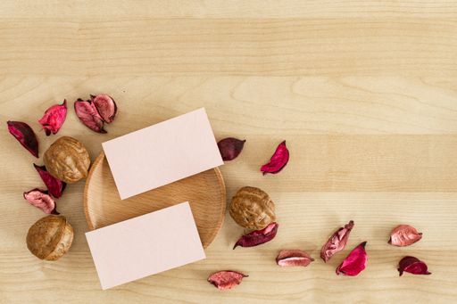 Two pink blank business cards and dry petals walnuts on a wooden office table mockup