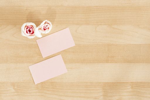 A top shot of two pink business cards and rose flowerheads on a wooden office desk mockup