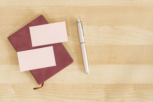 Two pink blank business cards on a notebook isolated on a wooden office table mockup