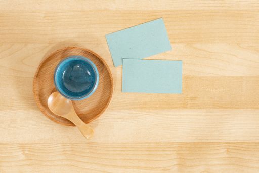 Blue carton recycled business cards next to a bowl with a spoon on a wooden office table mockup