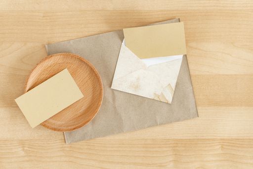 A blank recycled paper visiting card with a rustic envelope on a wooden office desk mockup