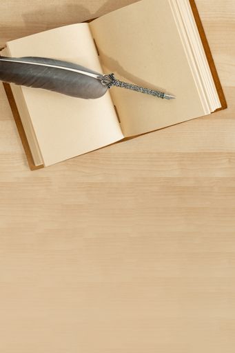 A decorated feather quill pen on an open handmade leather notebook isolated on a wooden desk mockup