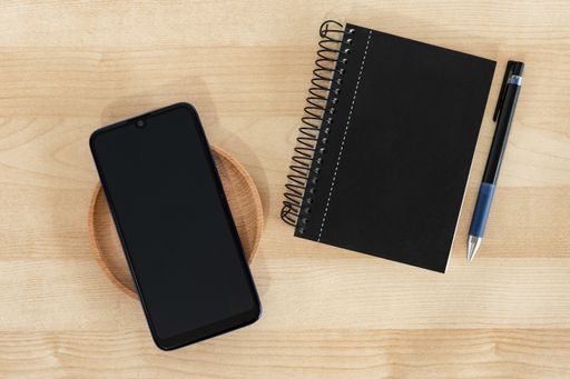 A top view of a black smartphone, notebook, and pen on a wooden background, office banner style