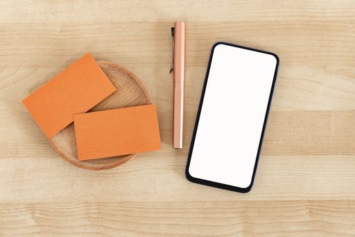 A top view of blank business cards and a smartphone on a wooden office table, recycled paper
