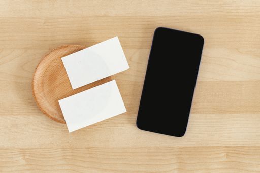 A top view of blank business cards and a smartphone on a wooden office table, recycled paper
