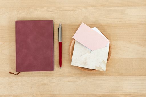 A notebook, pen, and pink blank business cards with a rustic envelope on a wooden desk mockup