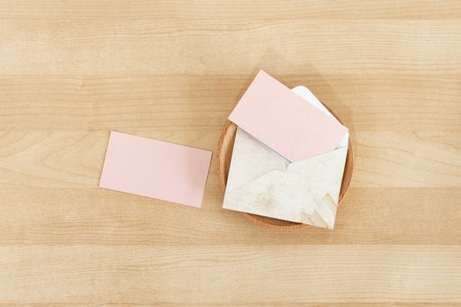 Two pink blank paper business cards with a rustic envelope on a wooden desk mockup