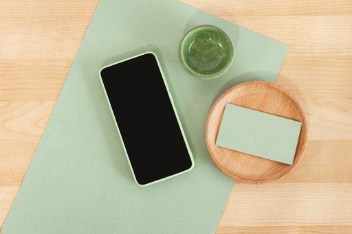 A smartphone with a blank screen next to a rustic carton recycled business card on a wooden desk mockup