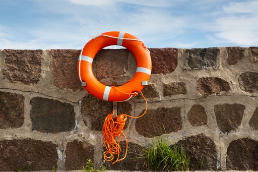 Orange life ring with leash is attached to brick wall in front of blue sky with clouds