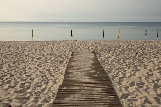 A closeup shot of a wooden walking path on sandy beach with closed umbrellas and the seascape