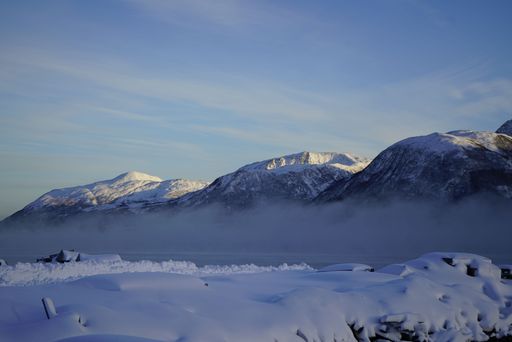 Snow-covered mountains with mist under a clear blue sky, showcasing a serene winter landscape.