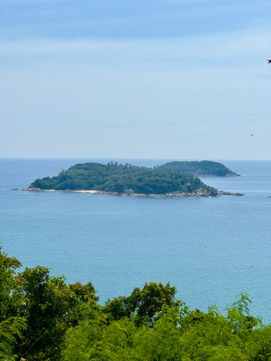 A scenic view of a lush green island surrounded by a clear blue ocean under a bright sky.