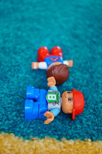 Lego Duplo boy figurines laying on  a carpet floor in soft focus.