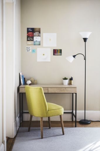 A vertical shot of a yellow chair and tall lamp near a wooden table with books and plant pots on it