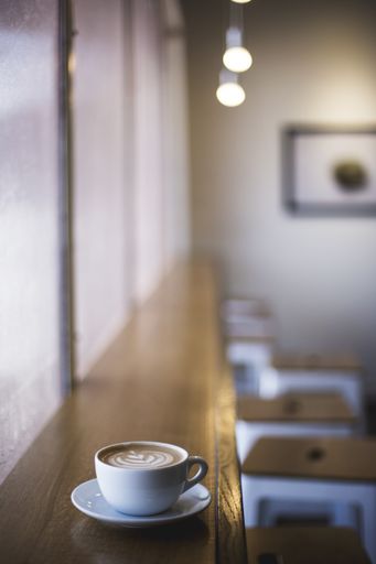 A vertical closeup shot of white cup of latte art coffee on a window shelf in a cafe