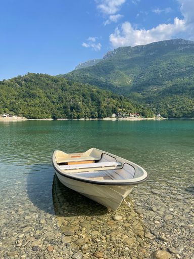 A vertical shot of a small white boat in a crystal water and a natural green mountain in the back
