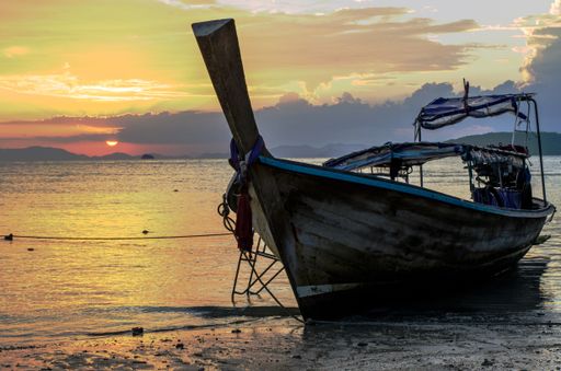 A closeup of a wooden boat on the beach surrounded by the sea under a cloudy sky during the sunset