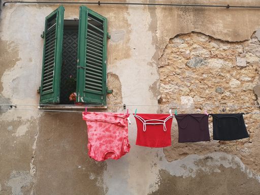 A closeup of the laundry drying on ropes on an old building with a wooden window