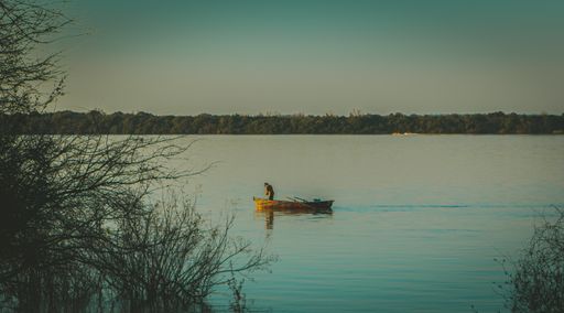 A shot of a person in an old yellow wooden boat floating in a lake during sunset