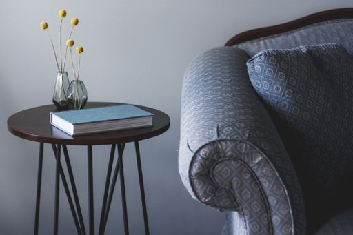 A shot of a blue sofa near a small round table with a book and two vases with yellow plants on it