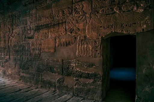 Ancient Egyptian hieroglyphics carved into temple walls with a mysterious doorway, showcasing historical artistry and architecture.