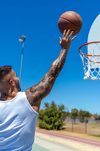 A vertical shot of a sporty Caucasian male with tattoos playing basketball