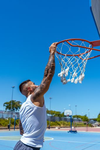 A vertical shot of a sporty Caucasian male with tattoos playing basketball