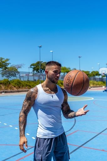 A vertical shot of a sporty Caucasian male with tattoos playing basketball
