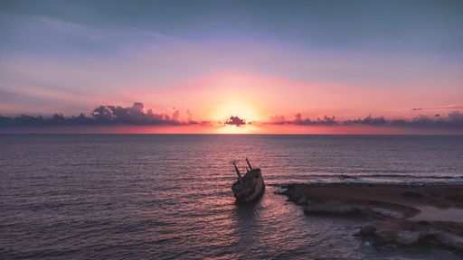 A stunning sunset over the ocean with a shipwreck on the coast, casting a serene and dramatic scene in vibrant colors.