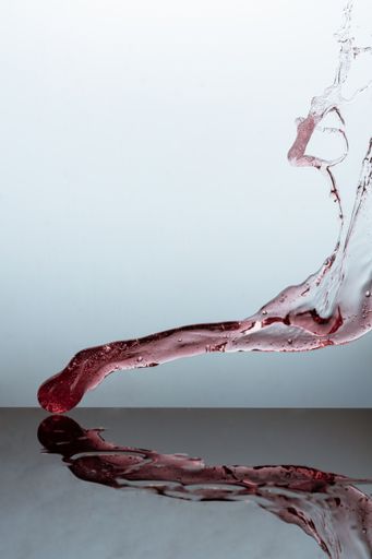 A vertical shot of wine splashing on a reflective glass surface against a gray background
