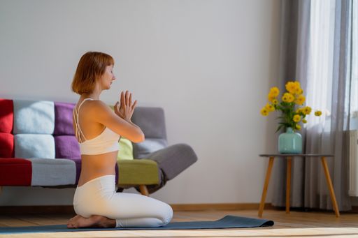 A side view of a Ukrainian young female in sportswear practicing yoga on the yoga mat at home
