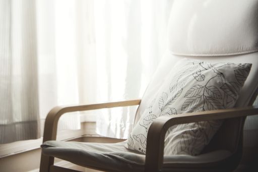 A closeup shot of a wooden white armchair with a white pillow on it