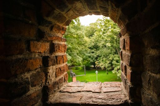 View through a rustic brick archway onto a lush green park, capturing a serene outdoor scene.