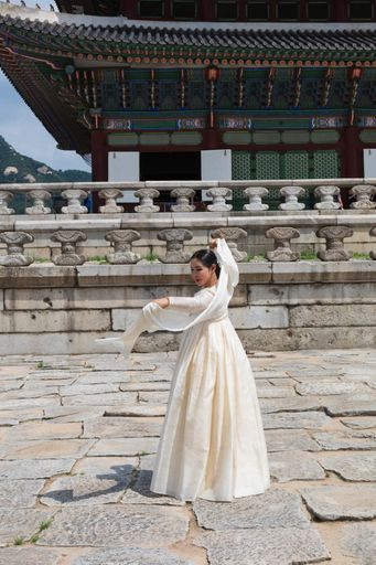 A South Korean young woman dancing in traditional Hanbok dress in Gyeongbokgung Palace, South Korea
