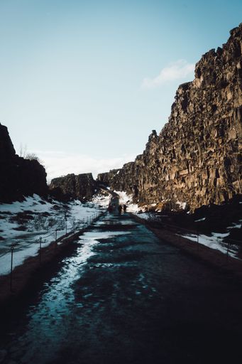 Scenic view of a rocky path through Thingvellir National Park, Iceland, with snow patches and a clear sky, capturing the rugged beauty of nature.
