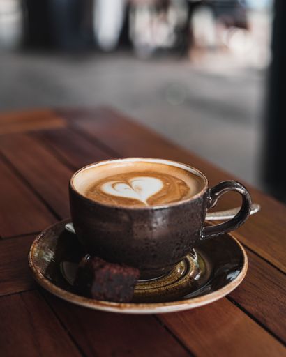 A closeup of a cup of fresh hot cappuccino with a piece of sweet pastry on the table in the cafe