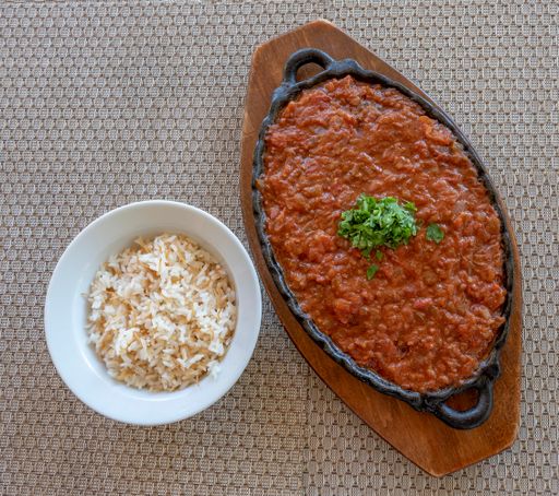 A top view of a red chutney Indian dish with green plant and rice on a little bowl on a decorated table