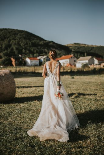 A vertical shot of a bride with a small bouquet in a field under sunlight