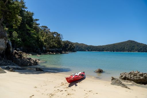 A serene beach scene with a red kayak on the sand, surrounded by lush greenery and calm blue waters under a clear sky.