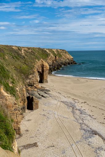 Scenic coastal view with sandy beach, rocky cliffs, and a clear blue sky, capturing the natural beauty of the seaside landscape.
