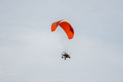 A paramotor with a bright orange wing soars against a clear sky, capturing the thrill of aerial adventure.