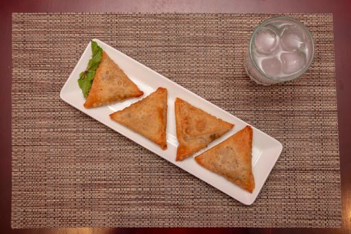 A top view of pita bread triangles with minced meat and a glass of iced drink on a red table