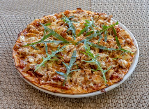 A close up of a pizza with sausage, cuisine sauce and rosemary served on a white plate on a gray surface
