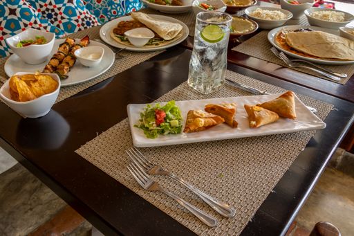 A close up of a table with  pita bread triangles, Shish taouk, water and cutlery